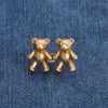 A pair of antique gold-toned bear button pins resting on a blue denim fabric.