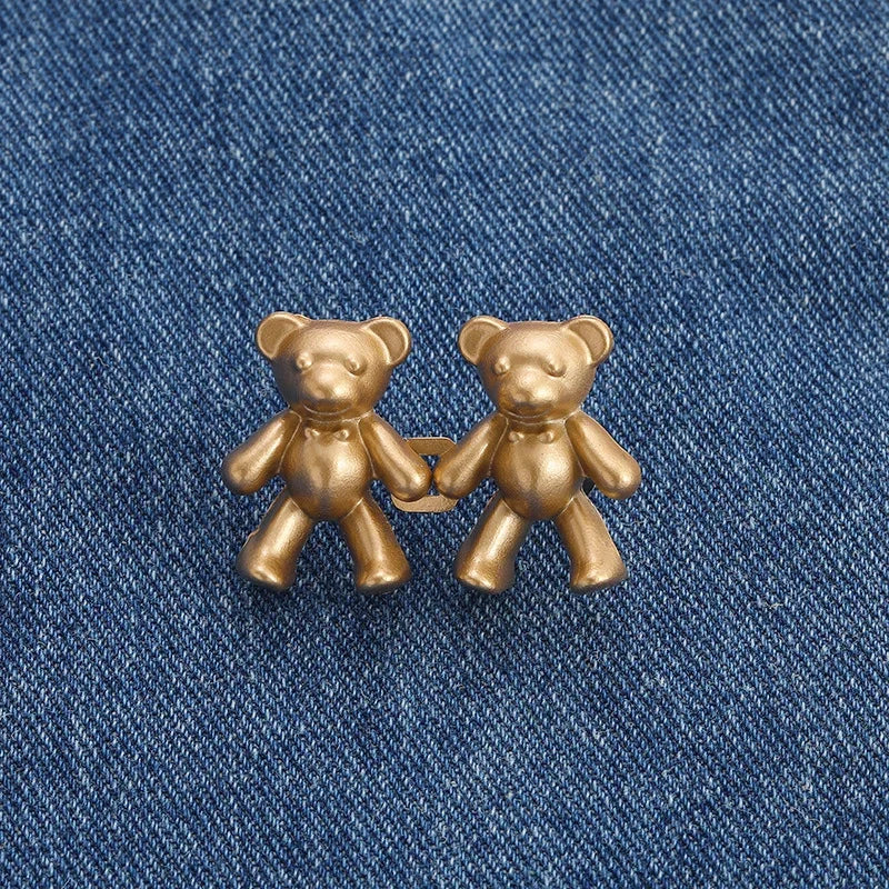 A pair of antique gold-toned bear button pins resting on a blue denim fabric.