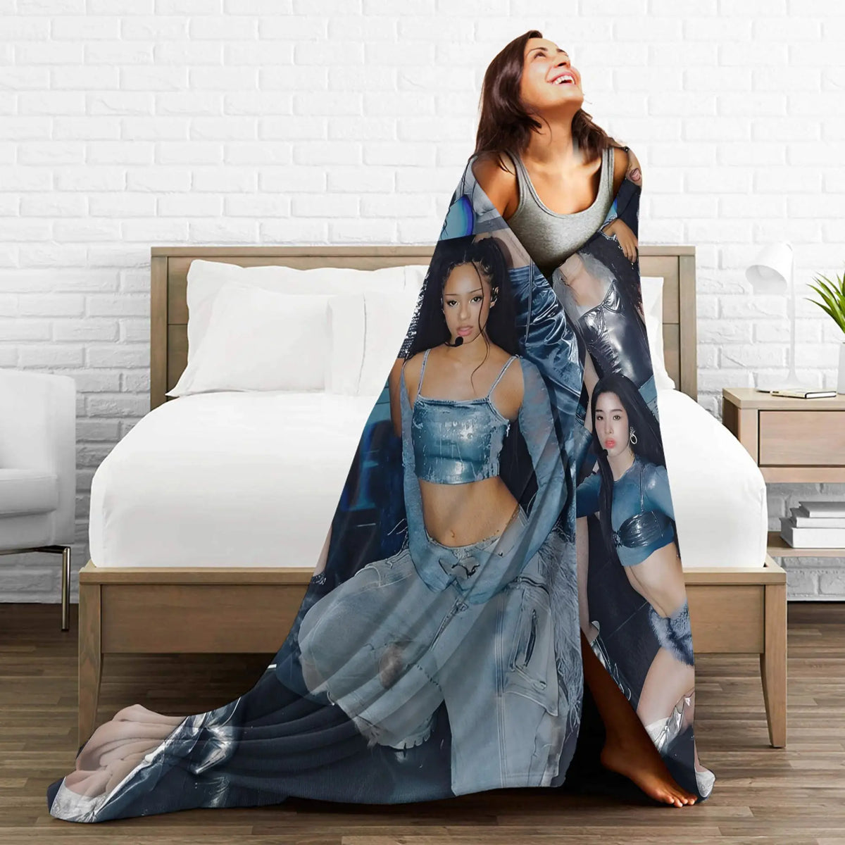A woman wearing a blue and gray K-Pop themed fleece throw blanket is lying on a bed.