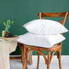 A white cotton-filled decorative throw pillow insert resting on a wooden chair against a dark green wall.