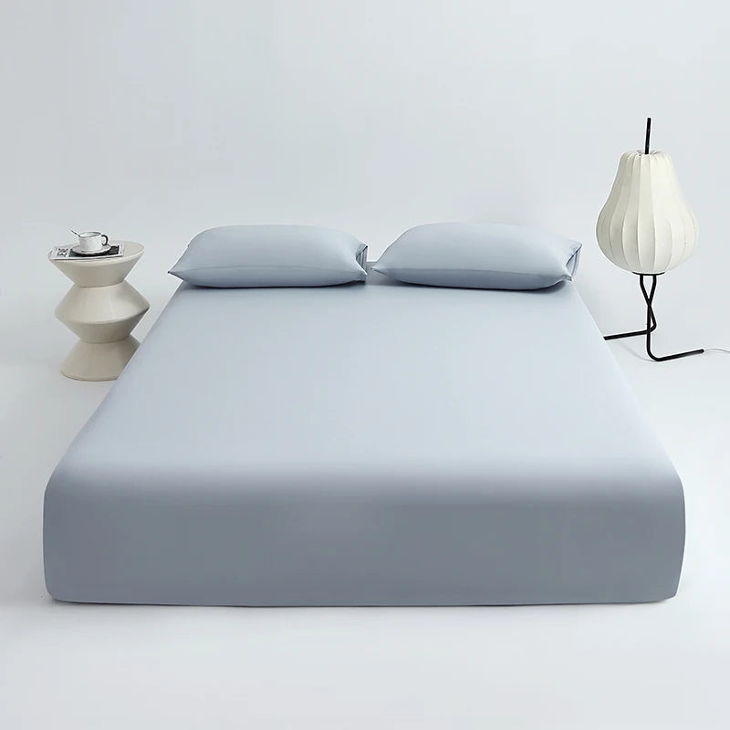 A light blue ice silk cooling fitted bed sheet set with two pillows and a modern lamp on a white surface.