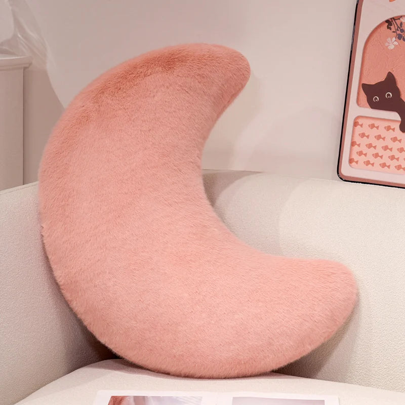 A soft, pink moon-shaped throw pillow resting on a white surface.