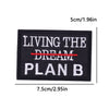 Black iron-on embroidery patch with white text reading LIVING THE DREAM PLAN B