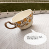 A ceramic cup with orange floral patterns rests on a white textured fabric.