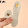 A hand holds a set of eight light beige leather bag buttons, some with gold accents.