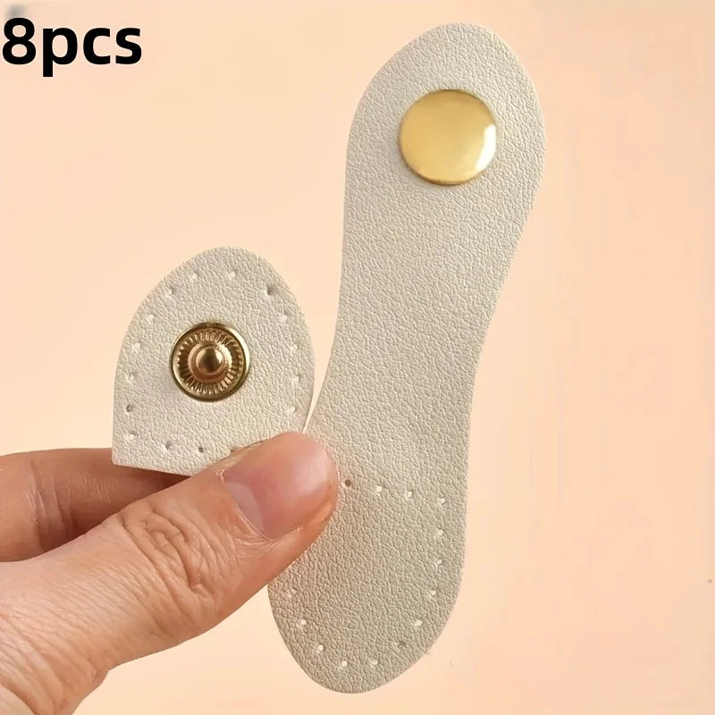 A hand holds a set of eight light beige leather bag buttons, some with gold accents.