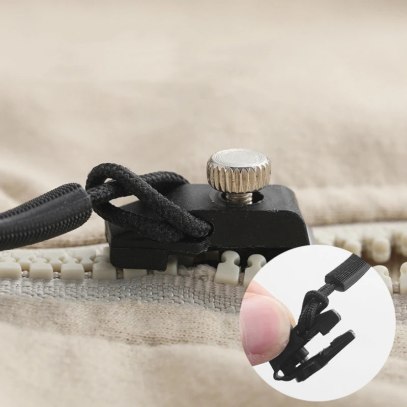 A black zipper repair kit with five detachable pulls is shown resting on a beige fabric surface.