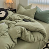 A light olive green duvet cover set with matching pillowcases and a black decorative pillow on a bed.