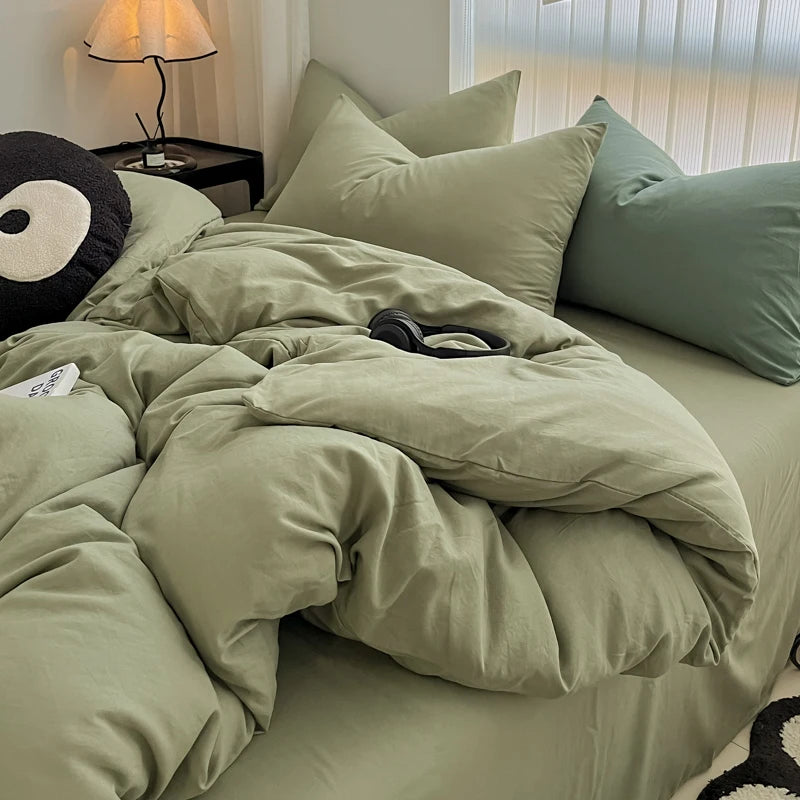 A light olive green duvet cover set with matching pillowcases and a black decorative pillow on a bed.