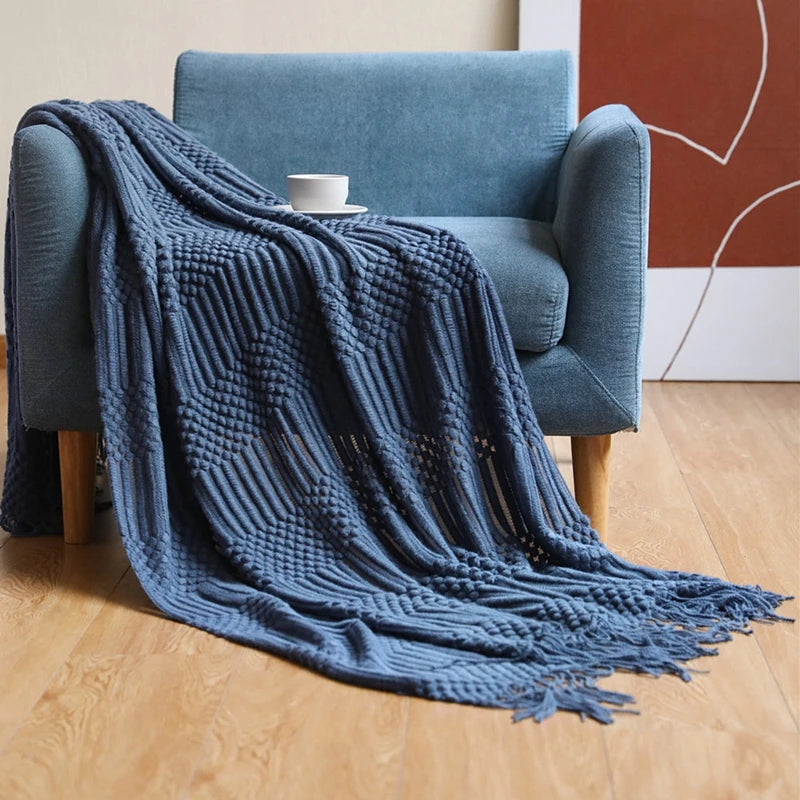 A deep blue oversized knitted tassel throw blanket draped over a light blue armchair.