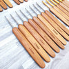 A set of wooden bamboo crochet and knitting needles with various sizes arranged diagonally on a light wooden surface.