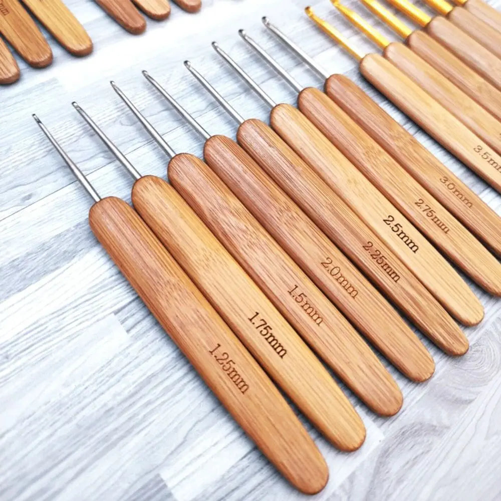 A set of wooden bamboo crochet and knitting needles with various sizes arranged diagonally on a light wooden surface.
