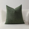 A textured, olive green decorative pillow cover with a quilted pattern resting on a white sofa.