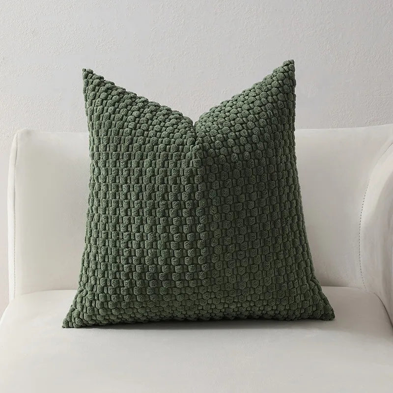 A textured, olive green decorative pillow cover with a quilted pattern resting on a white sofa.