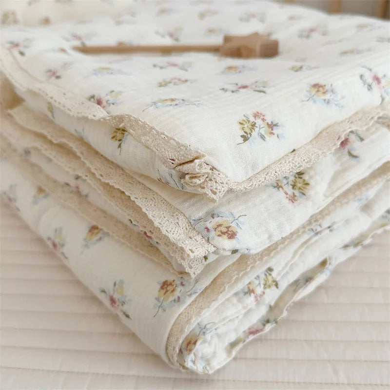 A stack of white muslin blankets with a floral print and delicate lace trim.