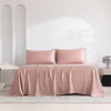 A pink luxury organic bamboo bed sheet set draped on a bed in a bright, minimalist room.