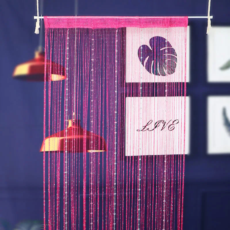 A pink beaded string curtain with tassels hangs against a dark blue background.