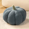 A round, fuzzy gray plush pumpkin throw pillow with a small green stem resting on a light beige surface.