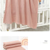 Pink all-season cotton baby swaddle blanket draped over a white wooden crib rail and folded neatly.