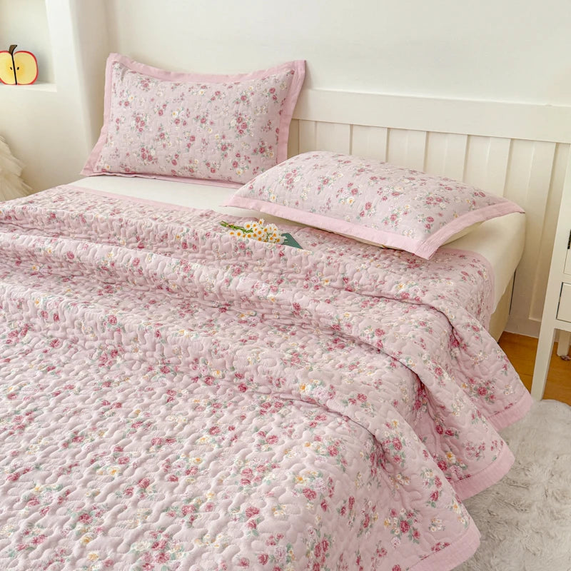 Pink floral quilted bedspread with a matching pillow on a white bed.
