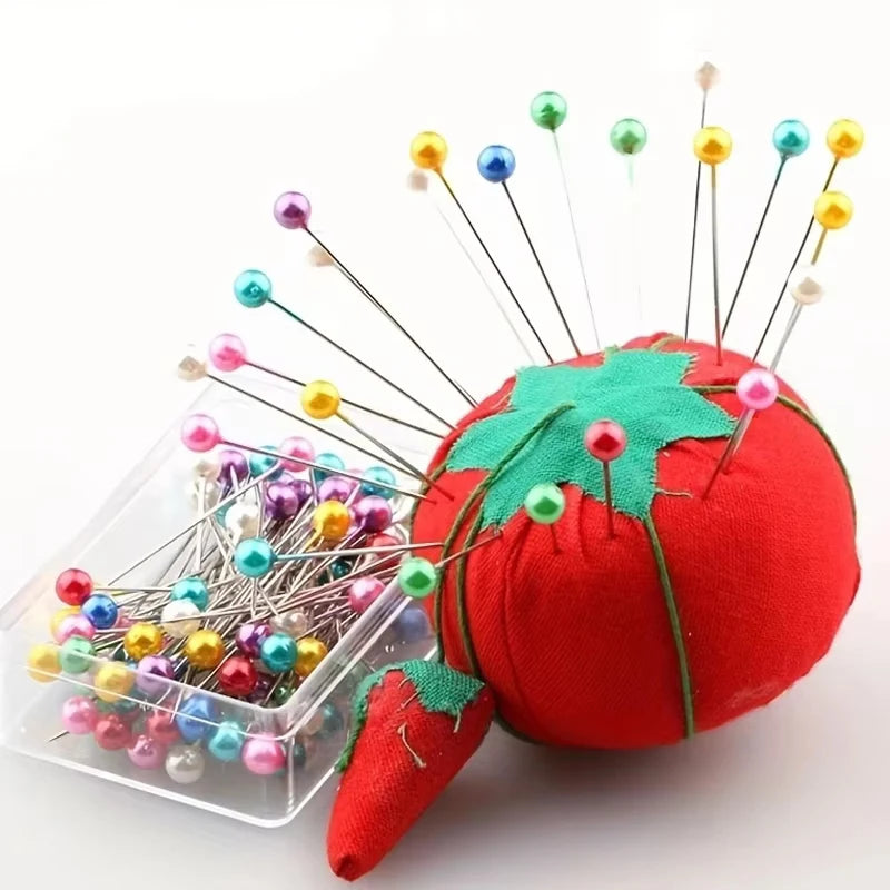A red fabric tomato with numerous decorative sewing and pinning needles topped with colorful beads.