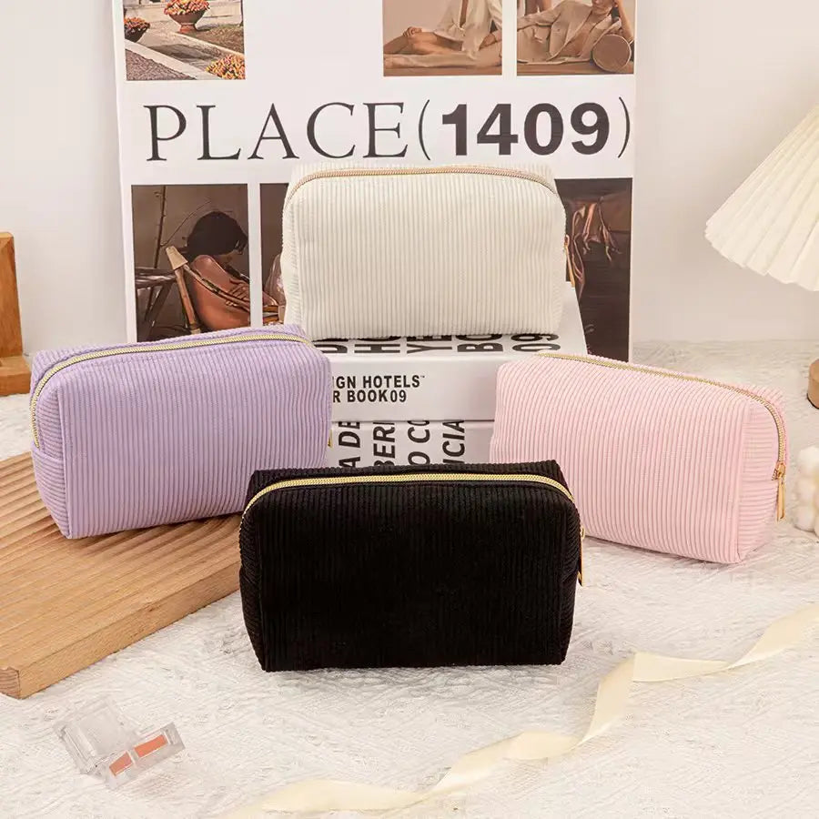 A collection of velvet cosmetic storage pouches in lavender, cream, and pink are displayed in front of a box.