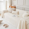 A cream-colored sofa covered with light beige pillows and a white blanket in a bright room.