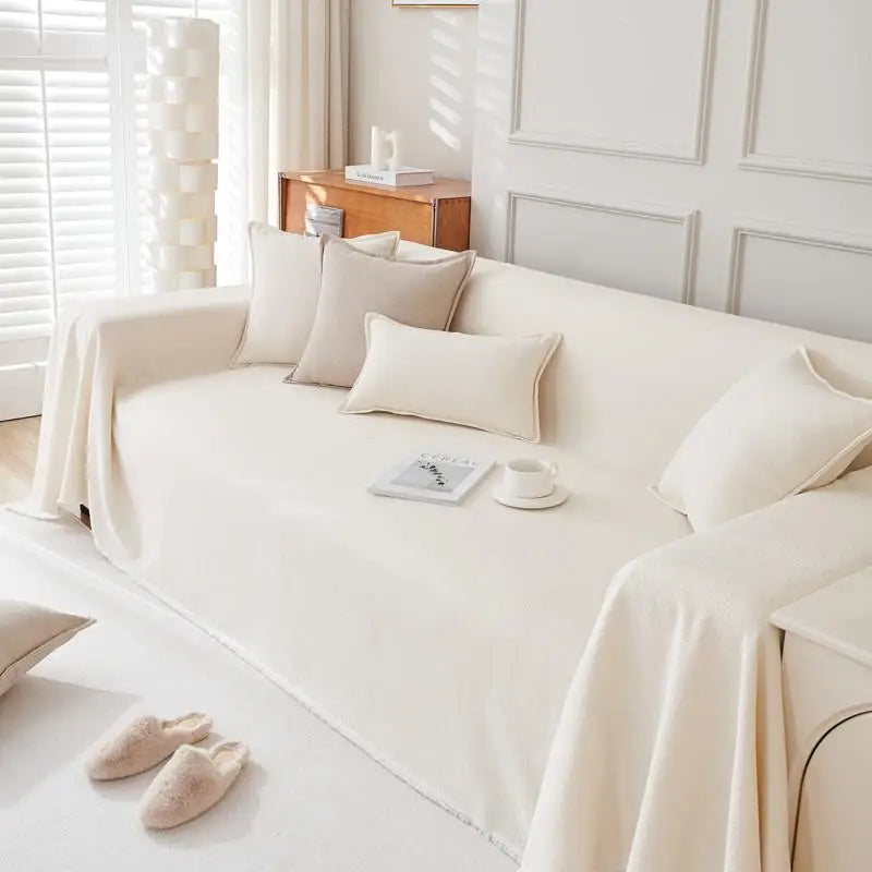 A cream-colored sofa covered with light beige pillows and a white blanket in a bright room.