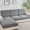A modern gray sofa with slipcovers sits in a bright living room next to a framed motivational sign and a potted plant.