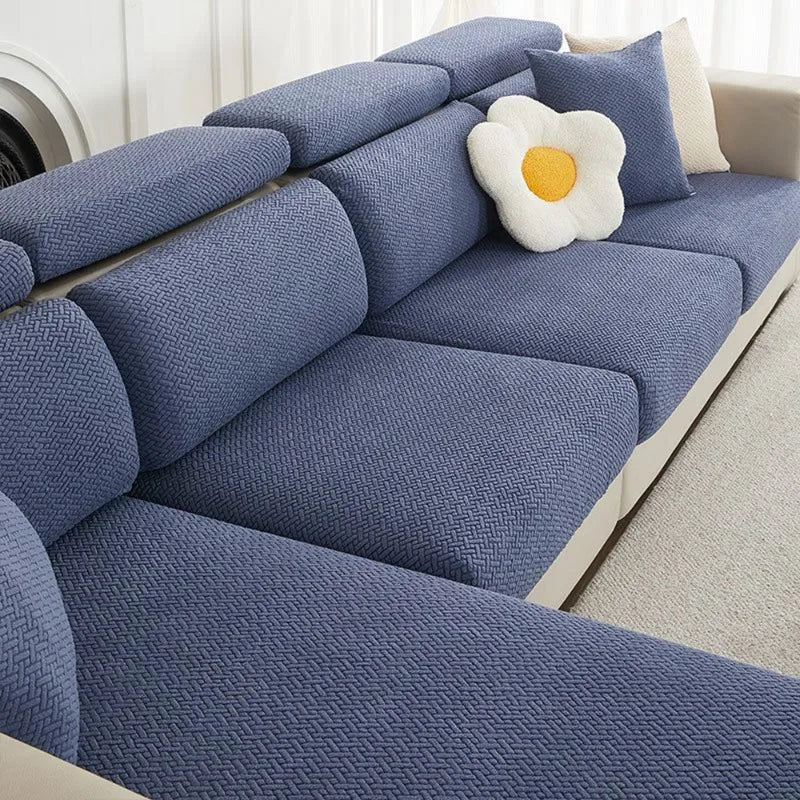 A navy blue jacquard elastic sofa cushion slipcover with a white flower accent on a light-colored sofa.