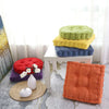 A stack of green and yellow tufted corduroy floor seat cushions next to a white stool and a single orange cushion.