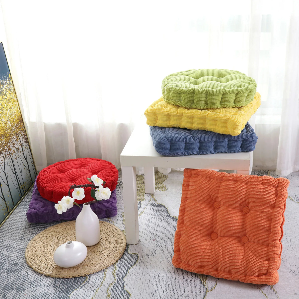 A stack of green and yellow tufted corduroy floor seat cushions next to a white stool and a single orange cushion.