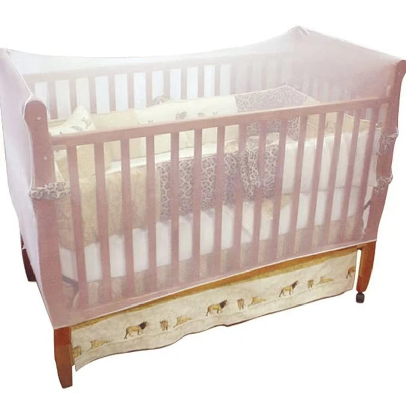A wooden crib with a sheer pink mosquito net covering the sides and top.