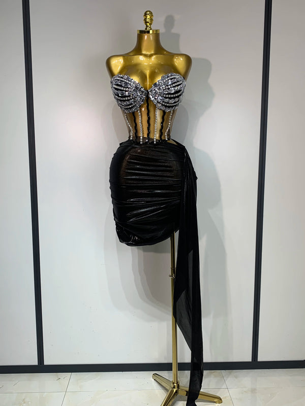 A gold mannequin displays a sparkly diamond two-piece performance set featuring embellished top and a black draped skirt.