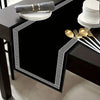A black placemat with a gold Greek key border and a gray napkin, set on a dark table.