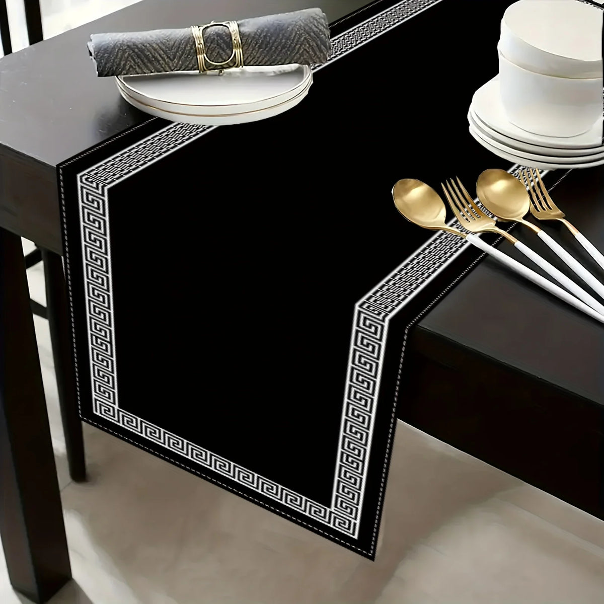 A black placemat with a gold Greek key border and a gray napkin, set on a dark table.