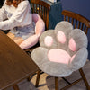 A soft gray plush bear paw cushion is shown on a wooden chair.