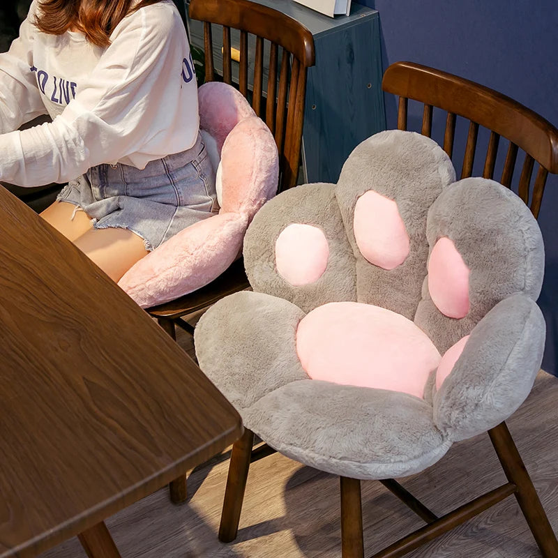 A soft gray plush bear paw cushion is shown on a wooden chair.