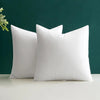 A pair of white polyester cushion inserts for throw pillows resting on a light surface against a dark green background.