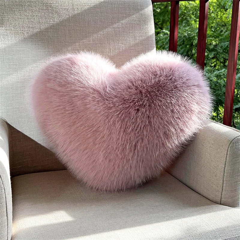 A fluffy pink heart-shaped fox fur throw pillow resting on a light-colored sofa.