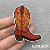 An embroidered patch of a brown cowboy boot with yellow stitching on a gray background.