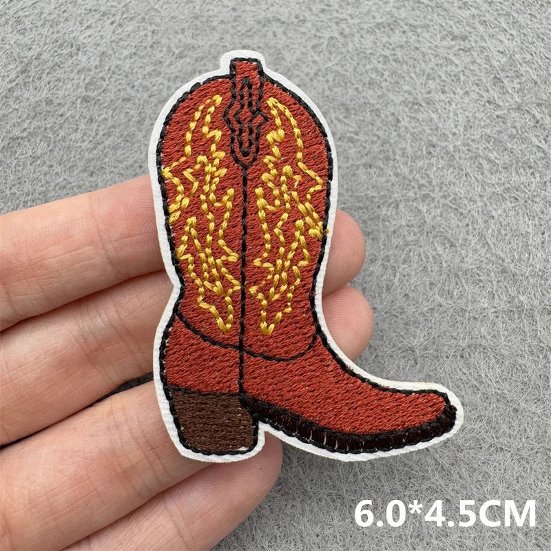 An embroidered patch of a brown cowboy boot with yellow stitching on a gray background.