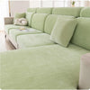 A light green universal elastic sofa cover with a full backrest and decorative pillows on a modern sofa.