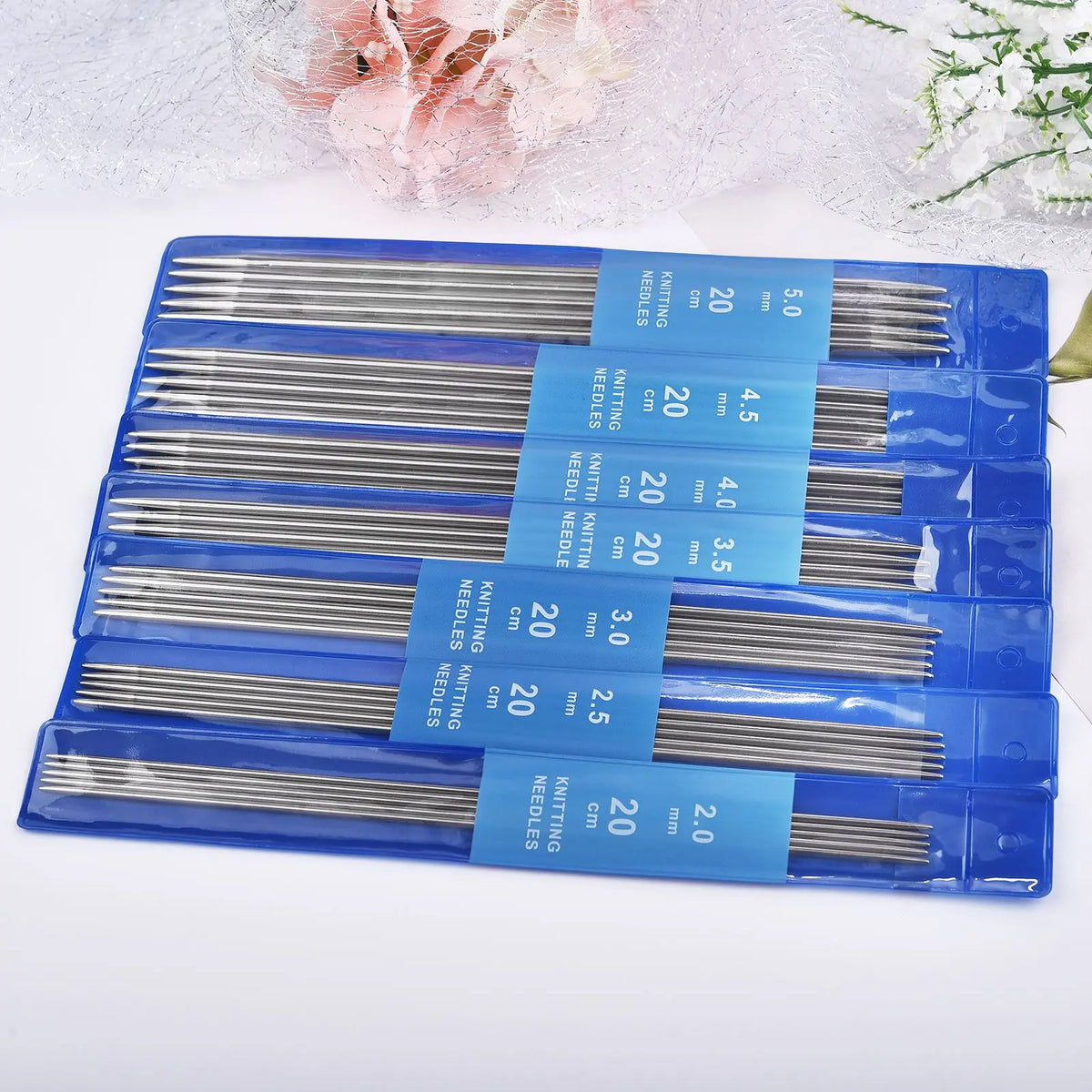 A set of blue plastic packaging containing various stainless steel knitting needles with different sizes and lengths.