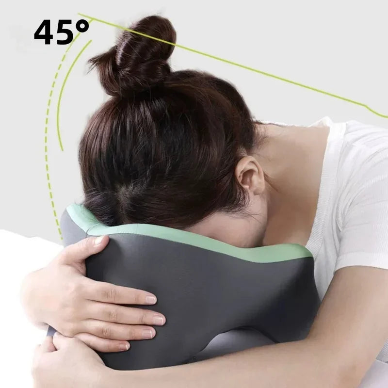 A person is using a gray memory foam U-shaped travel neck pillow for neck support, shown at a 45-degree angle.
