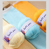A close-up of various skeins of soft yellow, light blue, and orange acrylic yarn laid out on a wooden surface.