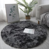 A round, dark gray shaggy area rug placed on a light wooden floor next to a potted palm plant and framed artwork.