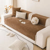 A beige sofa covered with a brown textured non-slip fabric and white decorative pillows.