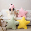 A person is sitting on a couch surrounded by various pink, yellow, and green star-shaped plush pillows.