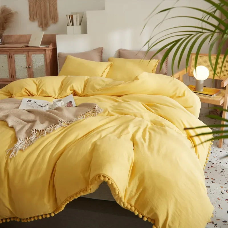 A bright yellow duvet cover set with pom-pom decoration displayed on a bed.